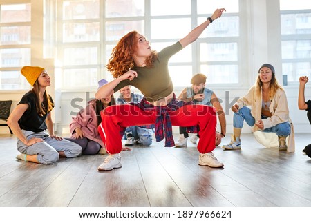 female dancer show her abilities in the studio, while other look at her moves. sportive youth gathered to train