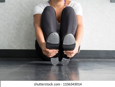 Female dancer sitting in tap class holding tap shoes