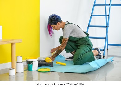 Female decorator with tape preparing wall for painting in room