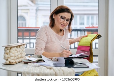 Female decorator working with samples of materials, making calculations, selecting fabrics and drawing models of curtains.