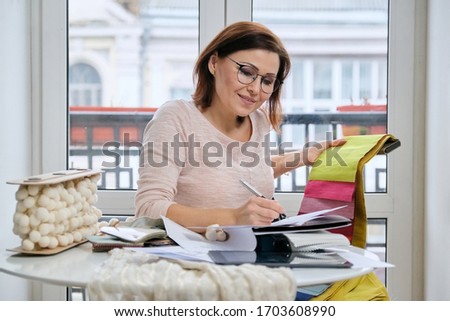 Female decorator working with samples of materials, making calculations, selecting fabrics and drawing models of curtains.