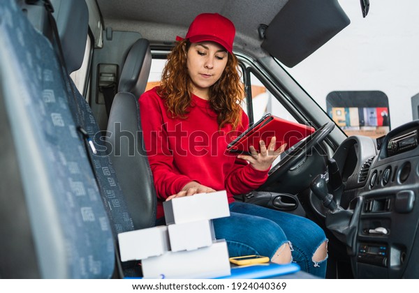 A female delivery driver tracking packages on a\
tablet in the van