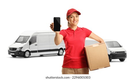 Female delivery worker in a red t-shirt holding a box and showing a mobile phone in front of transort vans isolated on white background 
