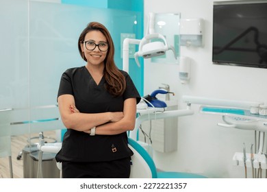 Female dentist with arms crossed looking at camera, standing in her medical office - Powered by Shutterstock