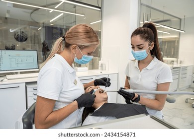 female dentist and an assistant treat the teeth of a young female patient. A dentist with an assistant at work in a dental office. Concept of dentistry and healthcare. - Powered by Shutterstock