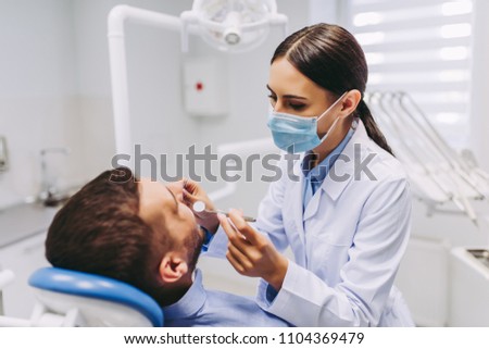 female dentist checking patient teeth with mirror in modern dental clinic