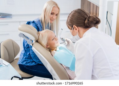 A Female Dentist Is Cleaning The Girl's Teeth With A Special Tool, The Girl Is Looking At The Doctor