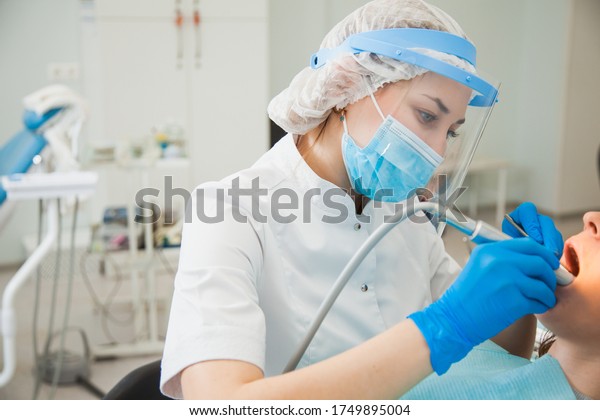 Female dentist curing\
teeth cavity in blue gloves and protective mask. Dentist caries\
treatment at dental clinic office. People, medicine, stomatology\
and health care concept