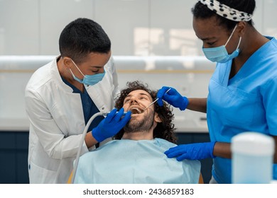 Female dentist is drilling man's tooth and healing caries while the nurse is assisting her. - Powered by Shutterstock