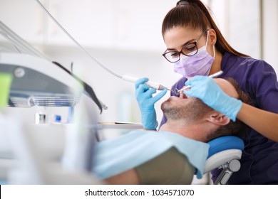 Female dentist drilling tooth to male patient in dental chair