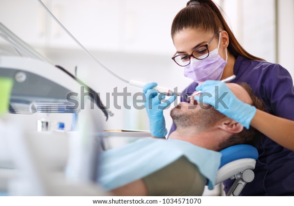 Female dentist drilling tooth to male patient in\
dental chair