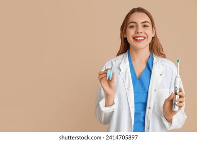 Female dentist with electric toothbrush and tooth model on beige background. World Dentist Day - Powered by Shutterstock