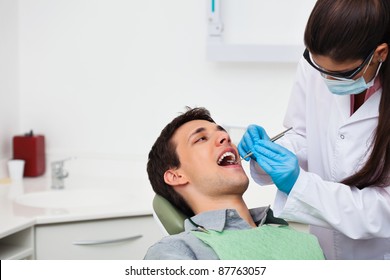 Female Dentist Examining A Male Patient At Clinic