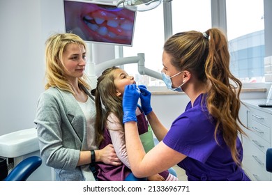 Female dentist examining teeth of little girl at dental clinic. Mother supporting her little daughter at dentist's office. Healthcare - Powered by Shutterstock