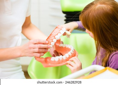 Female Dentist Explaining Girl Cleaning Tooth With Toothbrush On Model 