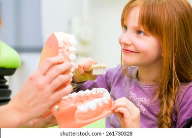 Female Dentist Explaining Girl Cleaning Tooth With Toothbrush On Model 