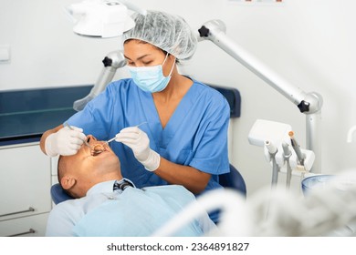 Female dentist in face mask inspects male patient teeth with mirror and probe - Shutterstock ID 2364891827