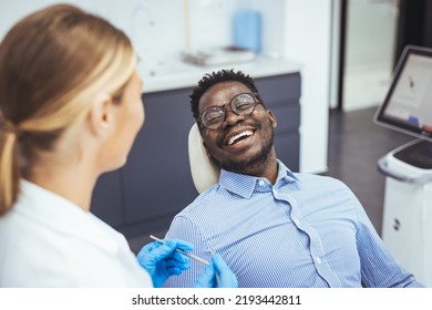 Female dentist with happy male patient at clinic. Happy patient sitting on chair while looking at dentist in medical clinic. Cheerful african american man with during examination in dental clinic - Powered by Shutterstock