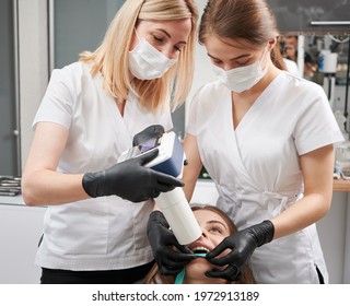 Female Dentist And Her Assistant Making X Ray Image With Portable X-ray Machine. People Wearing Clinic Uniform, Face Masks And Black Gloves. Concept Of Digital Dentistry And Intraoral Radiography.