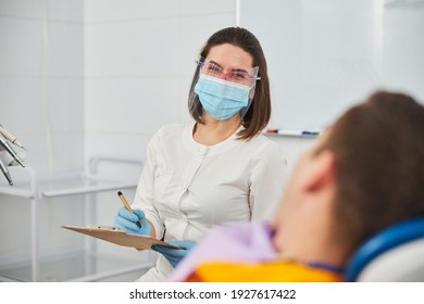 Female Dentist Laughing After Hearing Something Funny From A Man In Operation Chair While Writing About His Case