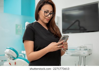 Female dentist looks at the screen of her cell phone while texting, in her medical office - Powered by Shutterstock