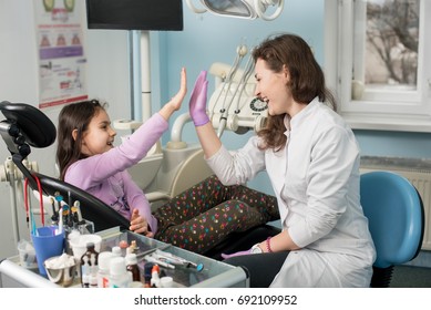 Female dentist and lovely kid after treating teeth at dental clinic office, smiling and giving high-five. Dentistry, medicine, stomatology and health care concept. Dental equipment