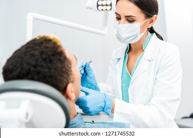 Female Dentist In Mask Examining African American Patient 