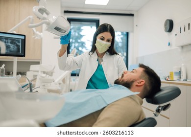 Female dentist positioning dental x ray equipment over male patient lying in dentist chair, preparing for dental examination in modern dental clinic