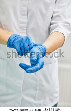 A female dentist puts on gloves against a background of dental equipment in a dental office. Happy patient and dentist concept.