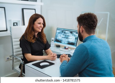 Female dentist showing x-ray footage of teeth to male patient in clinic - Powered by Shutterstock