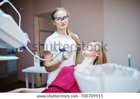 Female dentist in special glasses treating her patient's teeth with dental instruments.