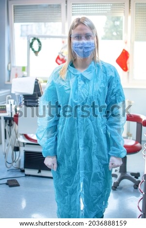 Female dentist in special protective clothes wearing Face Shield and Mask standing in dental office