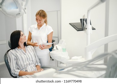 Female Dentist Talking With Patient Girl At Dental Clinic Office. Dentist Writing Prescription To Patient