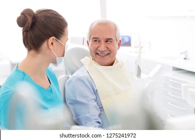 Female Dentist Talking To Smiling Senior Patient At Dental Clinic