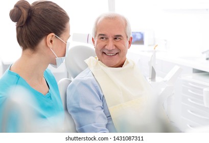 Female Dentist Talking To Smiling Senior Patient At Dental Clinic