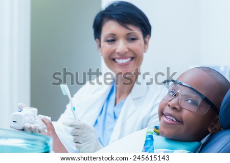 Female dentist teaching boy how to brush teeth in the dentists chair