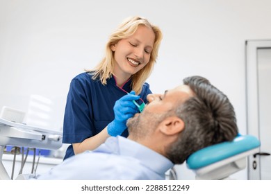 Female dentist treating teeth to patient, mid age man in chair at dental clinic. Dentistry, healthy teeth, medicine and healthcare concept - Powered by Shutterstock