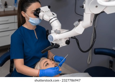 Female dentist using dental microscope treating patient teeth dental clinic office. undergoing treatment by experienced dentist using microscope. Image of woman on patient's chair in dentist's office. - Powered by Shutterstock