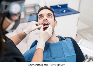 Female Dentist Wearing Face Shield Isolation Mask Working With Male Patient And Putting Teeth Covers.