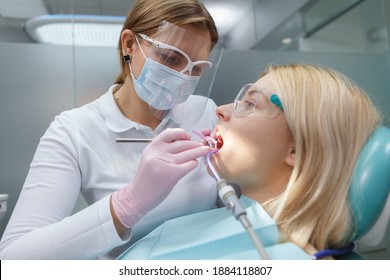 Female Dentist Wearing Protective Face Mask, Treating Teeth Of Female Patient