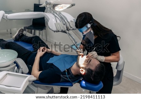 Female dentist wearing protective face mask working with young man during checkup revision.