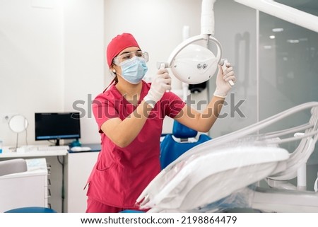 Female dentist working in modern dental clinic and wearing face mask. She is also wearing dental safety glasses.