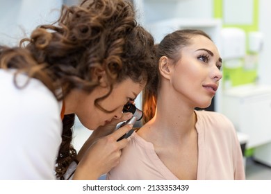 Female dermatologist carefully examining the skin of a female patient using a dermascope, looking for signs of skin cancer. Dermatologist examining patient's birthmark with magnifying glass in clinic