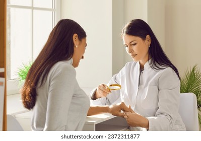 Female dermatologist examining skin of woman patient with magnifying glass. General practitioner doing skin examination in dermatology clinic. Professional doctor checking benign moles on arm - Powered by Shutterstock