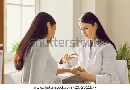 Female dermatologist examining skin of woman patient with magnifying glass. General practitioner doing skin examination in dermatology clinic. Professional doctor checking benign moles on arm