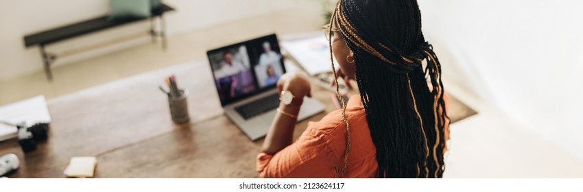 Female Designer Attending A Virtual Meeting With Her Clients. Young Female Freelancer Using A Laptop For A Video Call. Creative Young Woman Working On A New Project In Her Home Office.