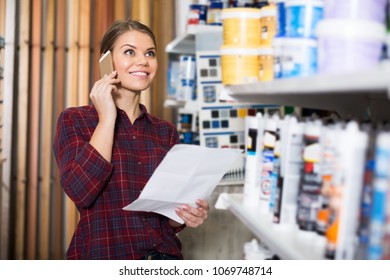 Female Designer Is Choosing Paint With List For Redecorate House And Talking By Phone In The Store