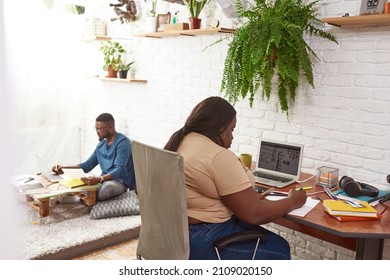 Female designer drawing paper at desk while blurred man in glasses using laptop computer at homemade table  Young black millennial couple working at home  Concept freelance   remote work