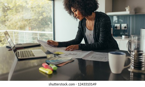 Female designer working at home office on new ideas. African woman sitting at her desk with laptop reviewing few documents. - Powered by Shutterstock