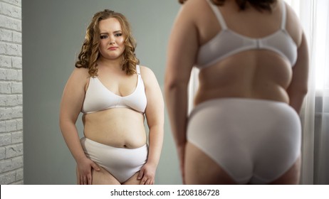 Female in despair looking at mirror reflection, ashamed of fat body insecurities